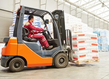 A man operating a forklift, carrying a palette of bags