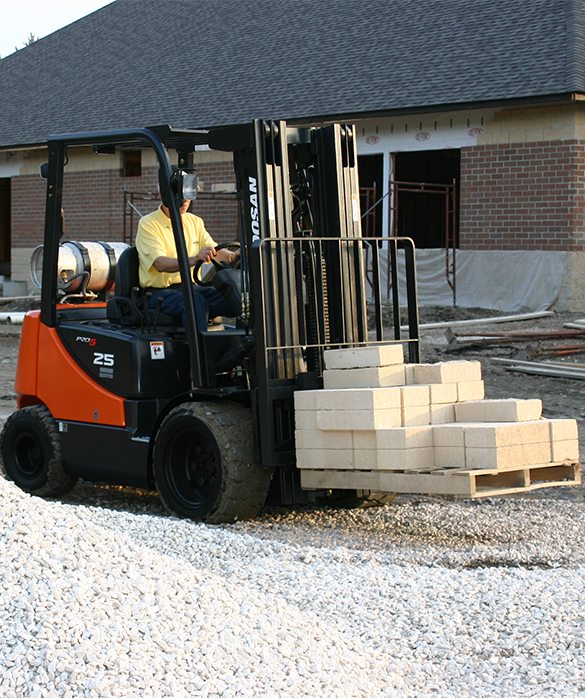 A man operating a forklift carrying concrete pavers
